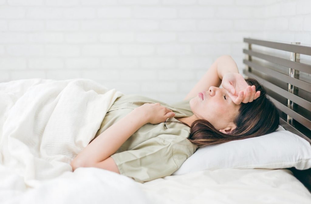 額に手を置きベッドで寝ている女性
